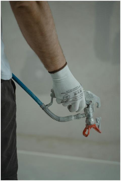 Arm of a worker holding a spray gun wearing gloves