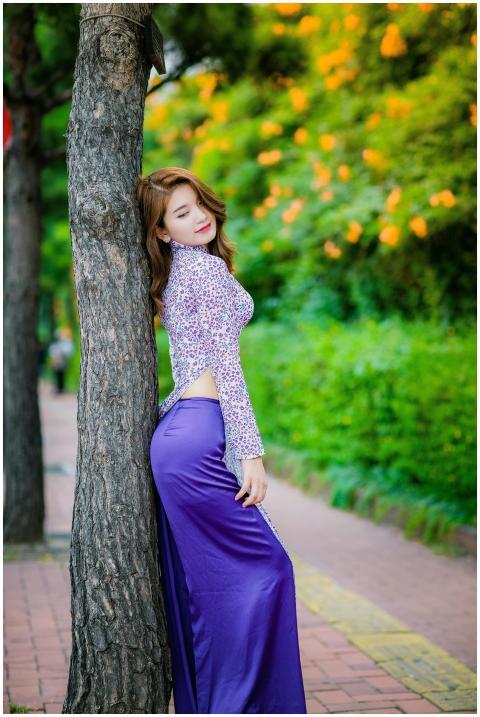 Stylish woman in a purple dress leaning on a tree