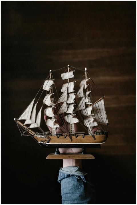 A hand in denim holds a vintage wooden model ship