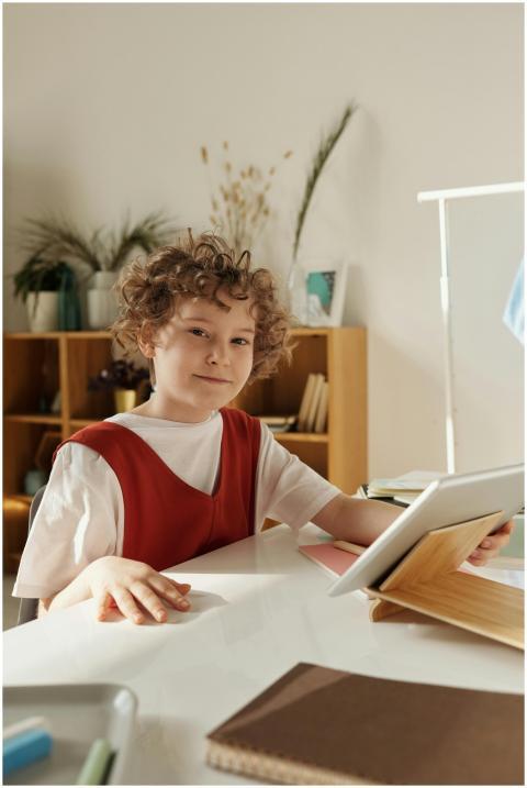 A cheerful boy in a red shirt studying on a tablet