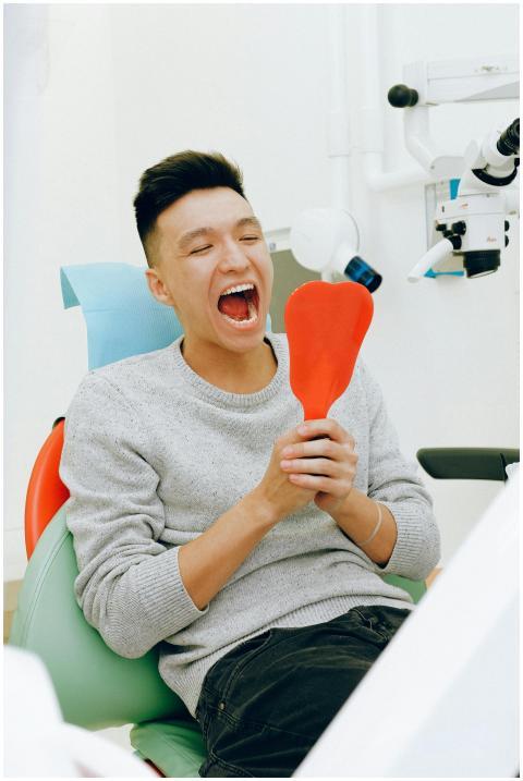 A man sits smiling in a dental clinic chair holdin