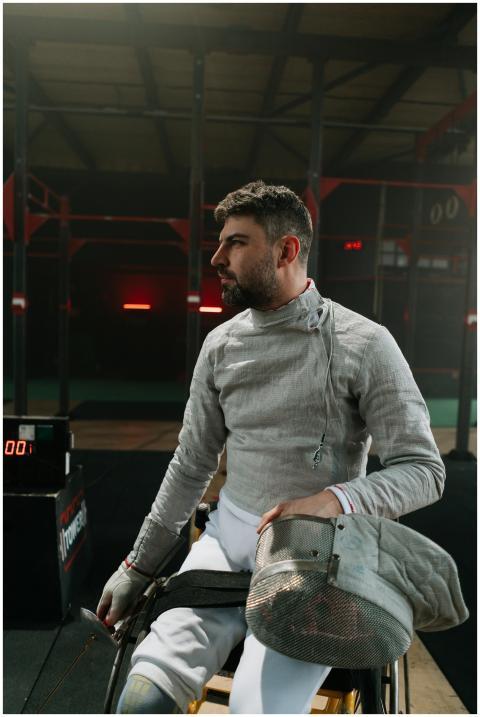 Male athlete in wheelchair fencing gear, indoors,