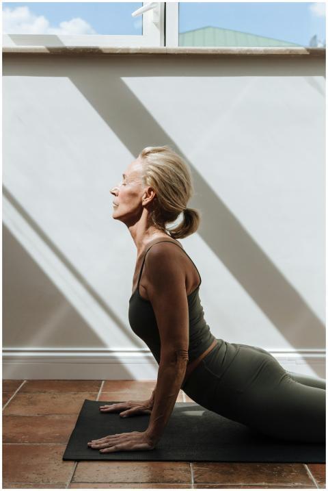 Elderly woman practicing yoga indoors with sunligh