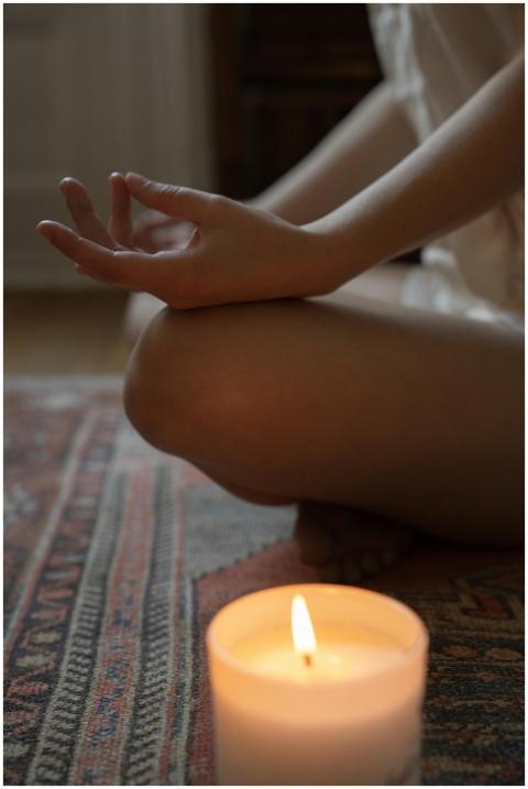 A person meditating indoors with a lit candle. Per