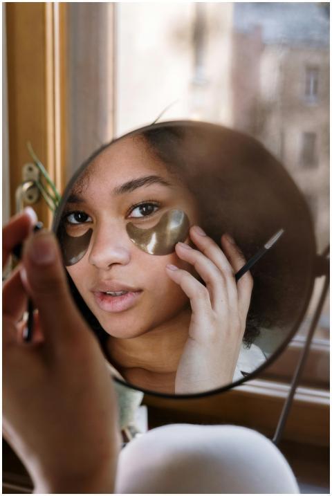 A woman with curly hair applies eye patches in fro