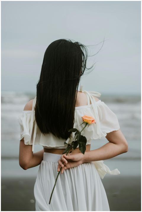 A woman with long hair holds a rose on a serene be