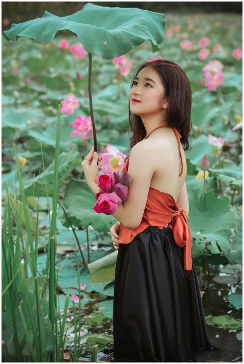 A stylish Asian woman stands amidst blooming lotus