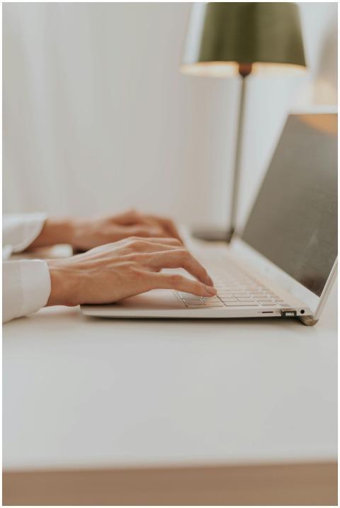 Close-up of hands typing on a laptop in a bright m