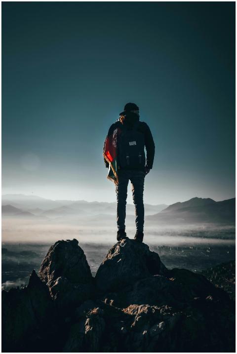 A lone hiker stands on a rocky peak, overlooking b