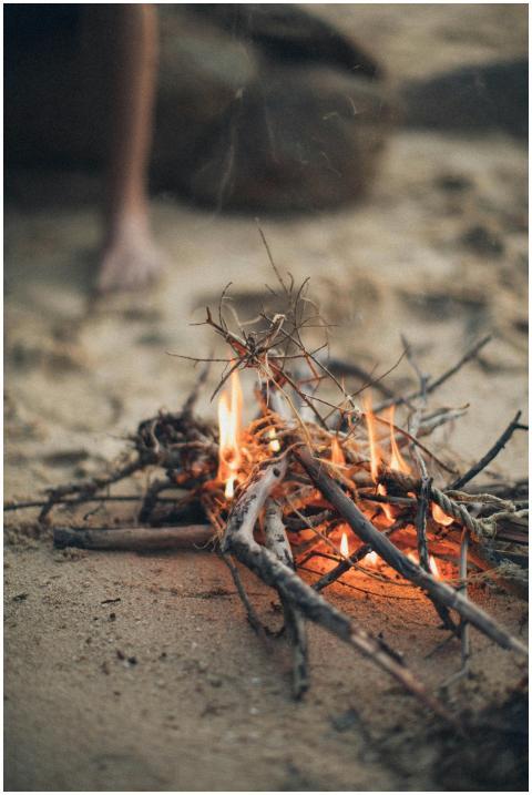 Close-up of a small campfire on a sandy beach, cre