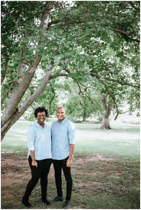 A happy couple stands together under a large tree