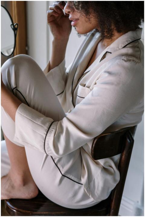 A woman in soft pajamas seated by a window, embrac