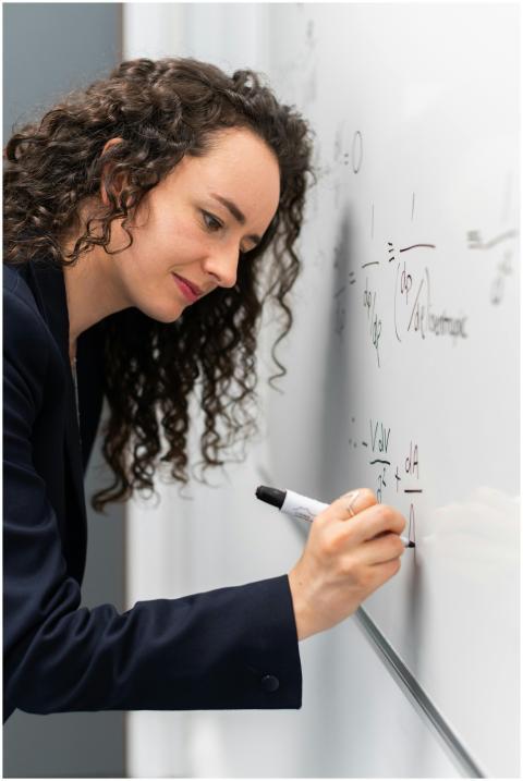 Female engineer solving equations on whiteboard wi