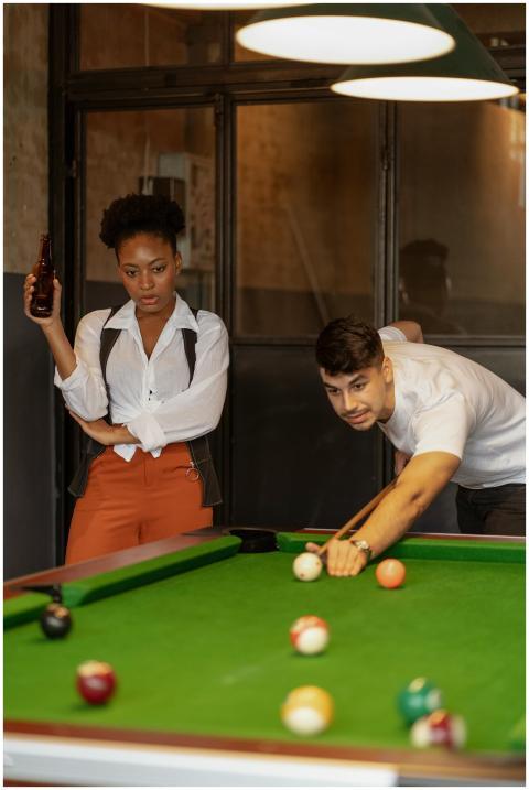 A woman and man enjoy a game of billiards indoors.