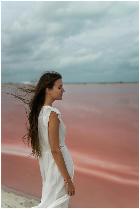 Woman in a white dress standing by a pink lake. Si