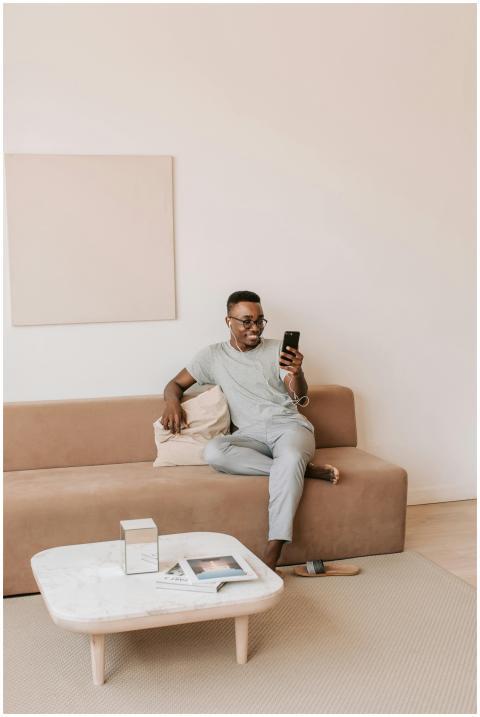 A man casually sits on a modern sofa using a smart