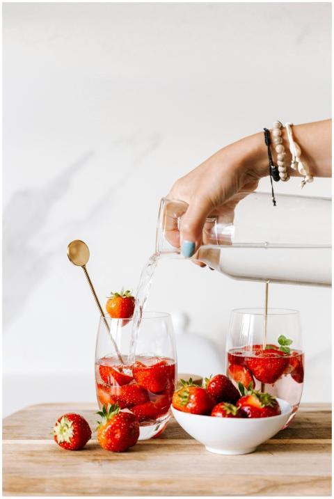 A hand pouring water into glasses with strawberrie