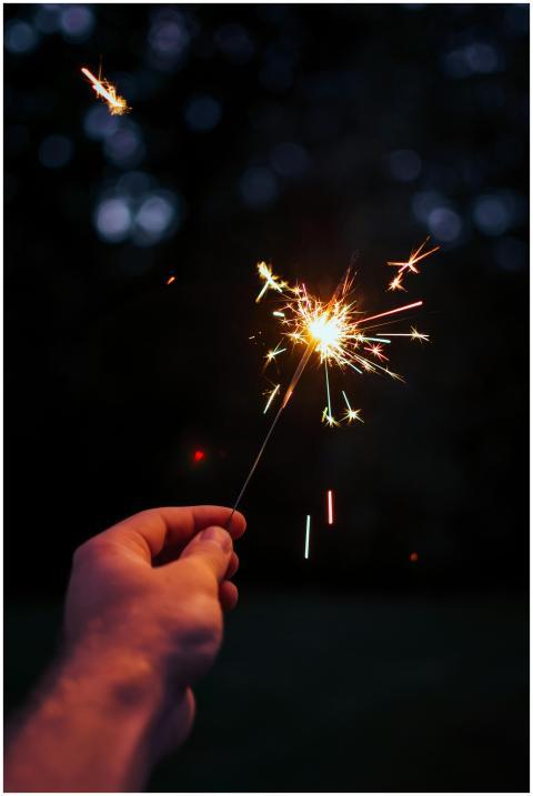 A person holding a bright sparkler outdoors in a f