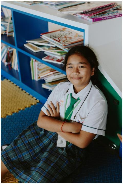 Happy girl in school uniform sitting in a library,