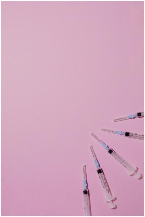 A collection of syringes arranged on a solid pink