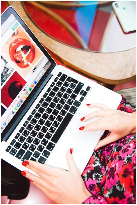A woman with red nails works on a laptop browsing