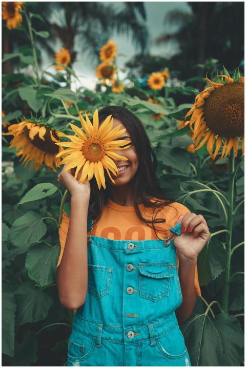 Joyful woman in denim holding sunflower among vibr