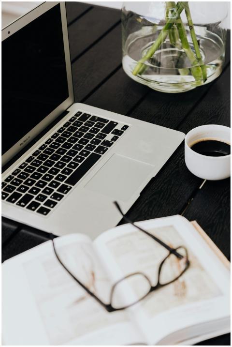 A tidy workspace with a laptop, coffee cup, open b