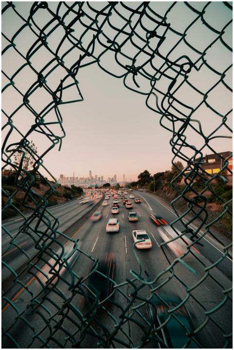 Traffic flows on a highway framed by a broken fenc