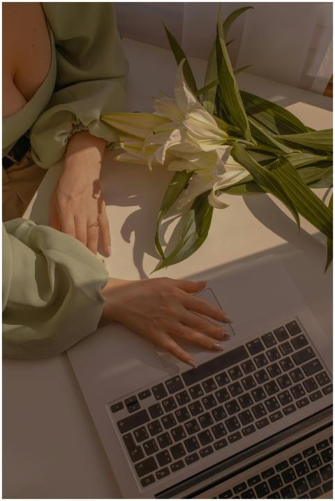 Woman's hands on a laptop with white lilies on a d