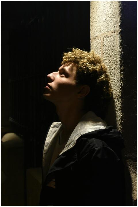 A young man with curly hair looks contemplatively