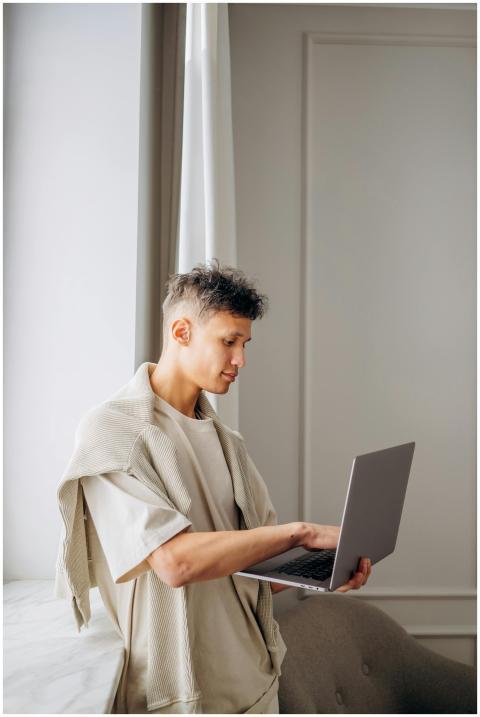 Young man standing by window using a laptop, captu
