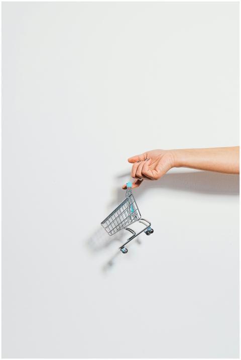 A hand holding a miniature shopping cart against a