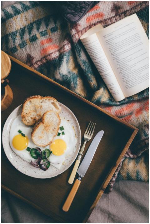 From above of opened book on bed near wooden tray