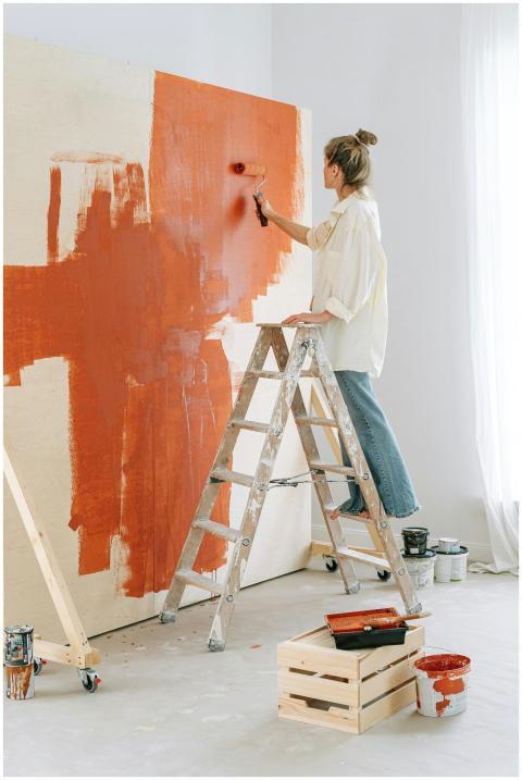 A woman stands on a stepladder, painting a room's