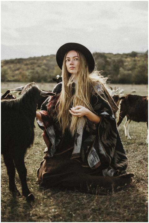 Woman wearing poncho and hat, surrounded by goats