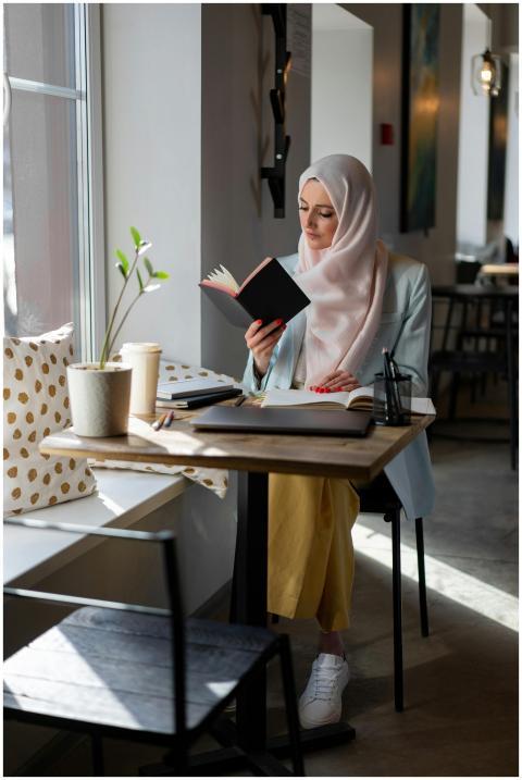 A young woman in a hijab reading a book at a cozy