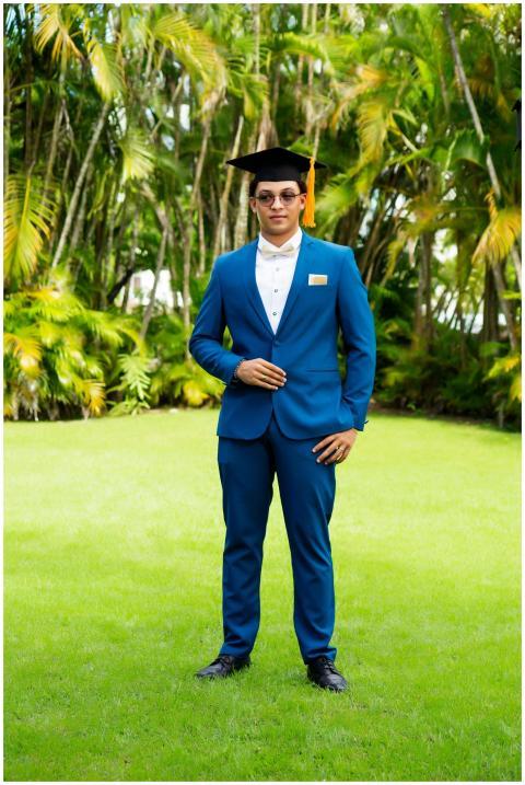A young man in a graduation cap and blue suit posi