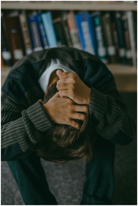 Person sitting with head down and hands on head in