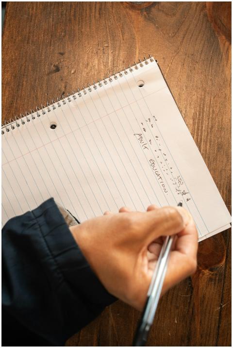 Close-up of a hand writing on a lined notebook wit