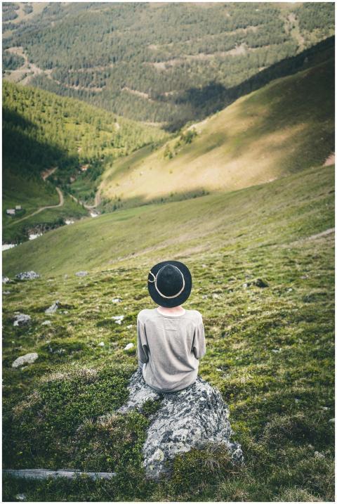 Individual in black hat seated on a rock, overlook