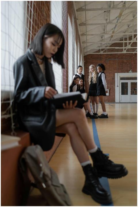Teen girl reading alone in gymnasium while peers w