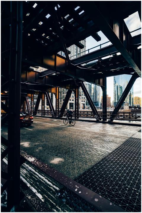 Metal bridge in a cityscape with cyclist and car p