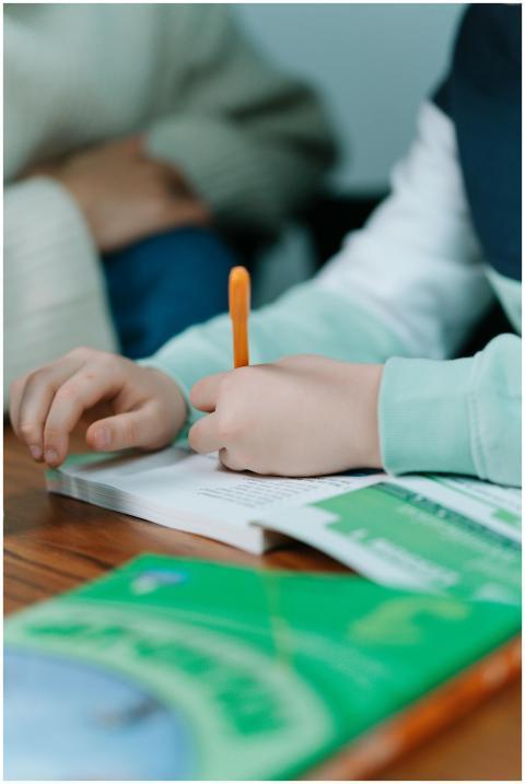 Close-up of a child's hands writing with an orange