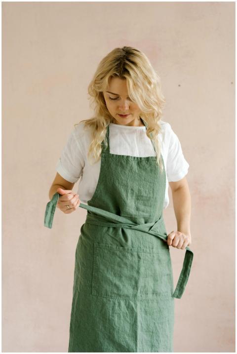 A woman in a green apron adjusts it, standing agai