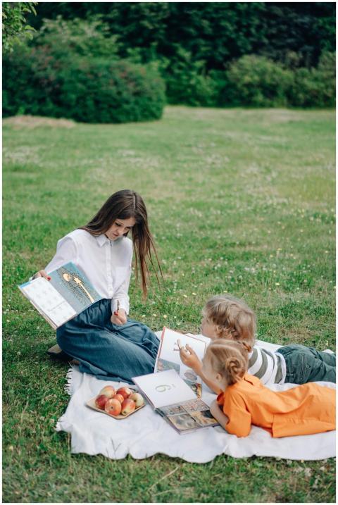 A woman reads to children on a picnic blanket with