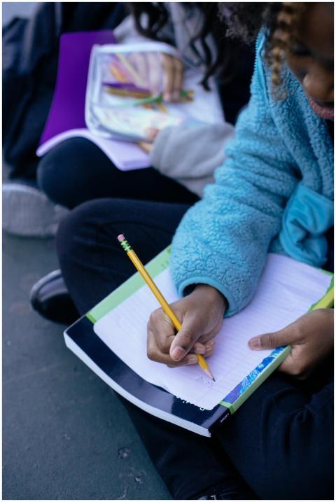 Child writing in a notebook outdoors, focusing on