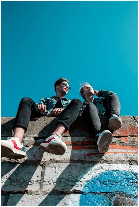 Two young people sitting on a stone wall under a v