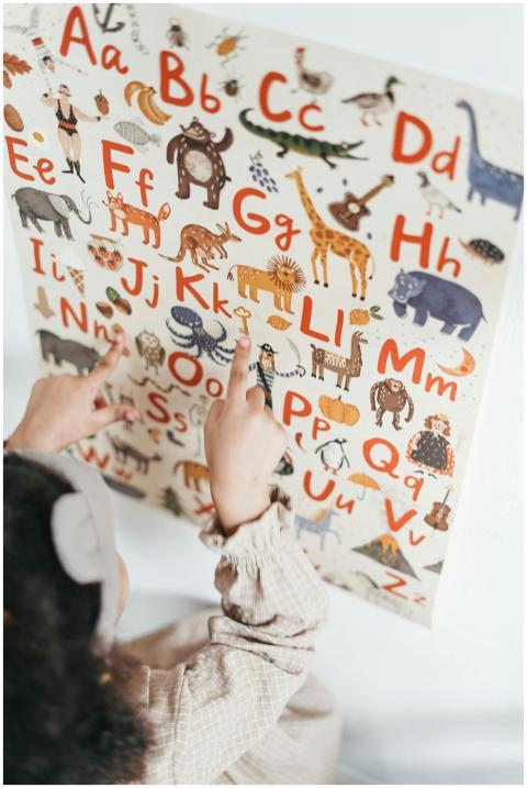A child points at an educational alphabet poster w