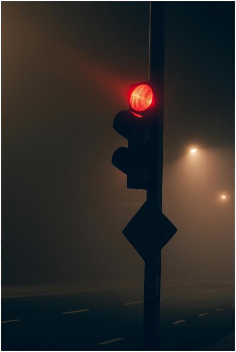 Red traffic light glowing in foggy night scene wit