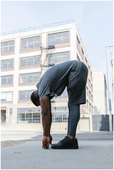 A man stretches outdoors near an urban building, f